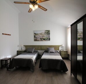 A bedroom with two beds, a ceiling fan, a painting on the wall, and a wooden floor.