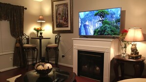 A living room with a fireplace, a television mounted above it, and a table with a bowl and remote controls.