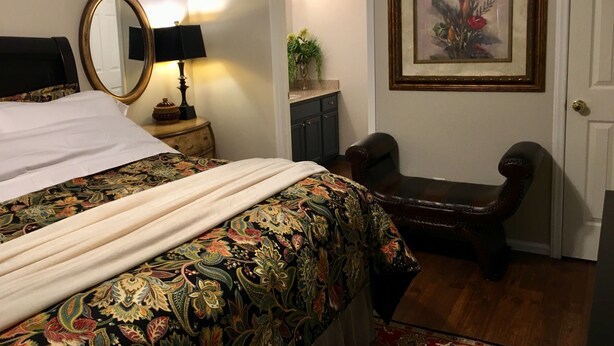 A bedroom with a bed, a chair, a desk, a mirror, and a framed picture on the wall.