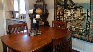 A dining area with a wooden table, chairs, and candles. There is a tapestry with a coastal scene on the wall.