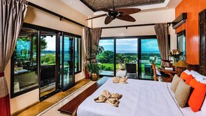 A spacious bedroom with a large bed, a ceiling fan, and a view of lush greenery and a distant cityscape through large sliding doors. - Casa Pipilacha♛Ocean view Infinity Edge Pool with  in-law suite♛ (Tamarindo)