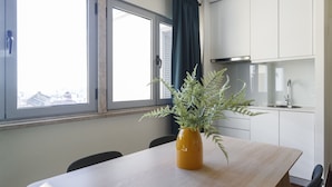 A modern kitchen with white cabinets, a stainless steel range hood, and a window with a view of buildings.