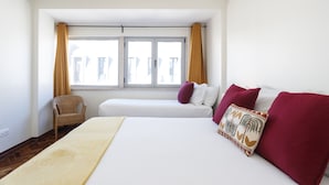 A hotel room with a large bed, a smaller bed, a chair, and a window with curtains.