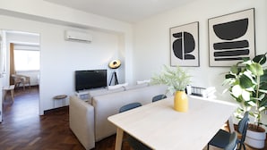 A modern living room with a sofa, a dining table, and a TV. There is a potted plant on the table.