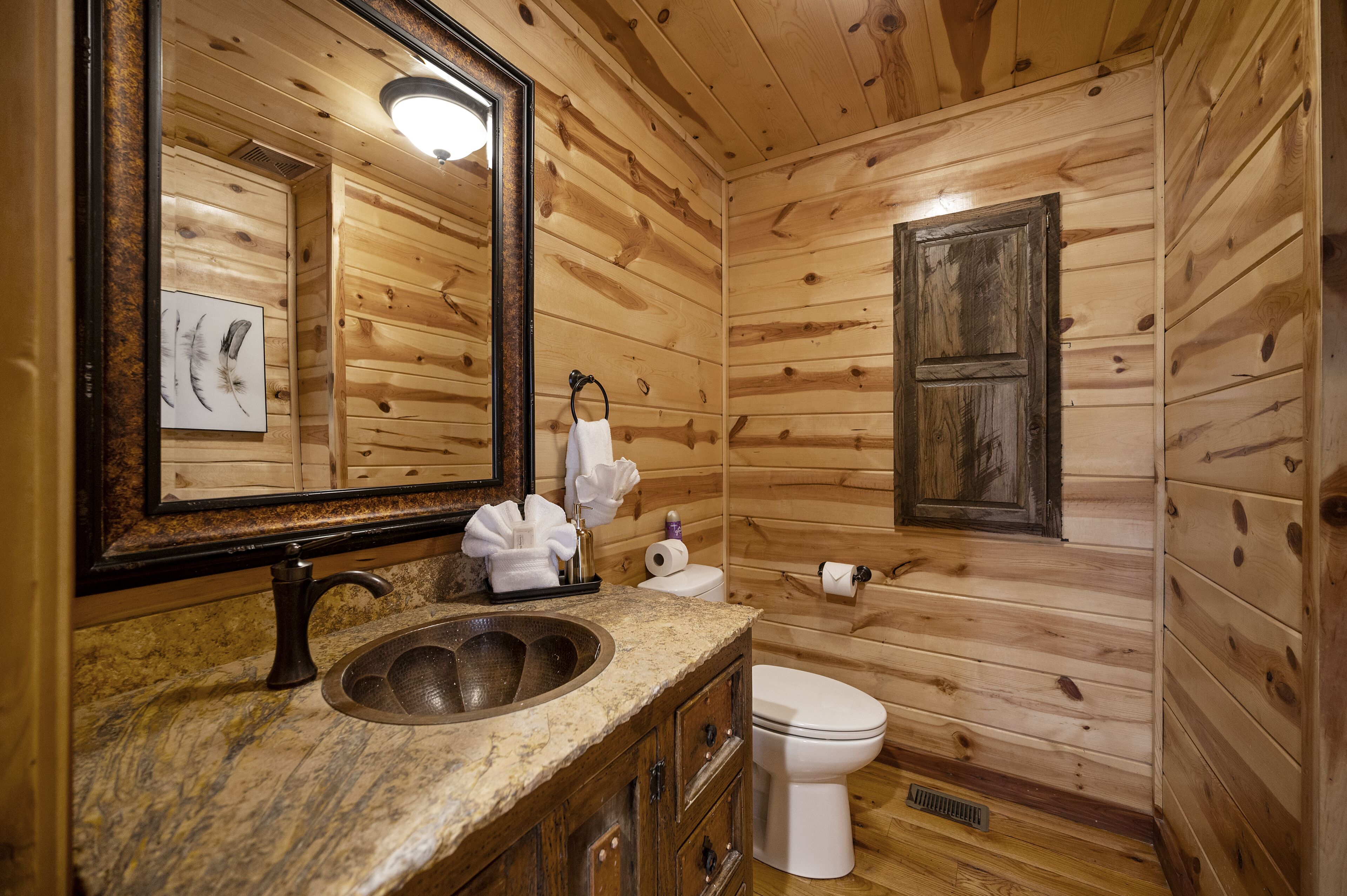 A wooden cabin bathroom with a granite sink, a toilet, and a mirror.