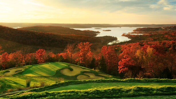 Un campo de golf con un lago y follaje otoñal.