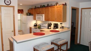 Una cocina compacta con muebles de madera, una encimera blanca y dos taburetes de bar.