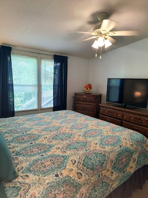 A bedroom with a large bed, a ceiling fan, a dresser, a TV, and a window with curtains.