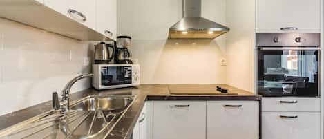 A modern kitchen with a stainless steel range hood, a built-in oven, a coffee maker, and a sink.