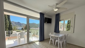 A room with a balcony, a dining table with chairs, a ceiling fan, and a TV mounted on the wall. - Agi Rescator 325 Apartamento for rent in Roses Girona. (Rosas / Roses)