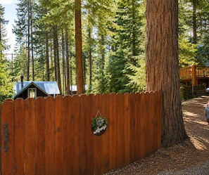 A wooden fence with a welcome sign, a tree, and a cabin in the background.