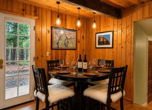 A dining area with a wooden table set for four, chairs with white fur throws, and two framed pictures on the wall.