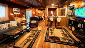 Acogedor interior de cabaña con sofá, sillas, una mesa de centro, televisor y una zona de bar.
