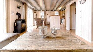 Ein gemütliches Interieur mit Holztisch, zwei Glasvasen, einem rustikalen Grill und einer Essecke mit Korbstühlen.