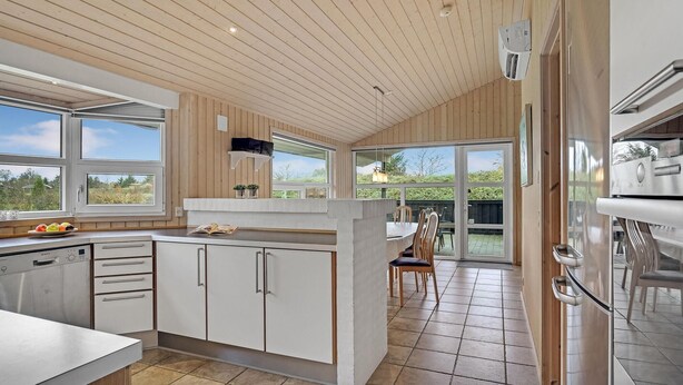 A modern kitchen with wooden paneling, a large island with seating, and a view to the outdoors. - Awesome home in Hovborg with sauna (Hovborg)