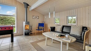 A cozy room with a wood-burning stove, a sofa, a coffee table, and a view of greenery outside. - Awesome home in Hovborg with sauna (Hovborg)