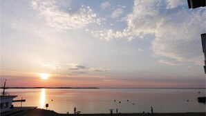Une scène de plage au coucher du soleil, avec une eau calme, quelques personnes et un bateau amarré sur la gauche.