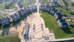 Une vue aérienne d’un quartier résidentiel composé de plusieurs maisons à deux étages, avec un espace central ouvert doté d’un élément circulaire, et une route qui traverse le quartier.