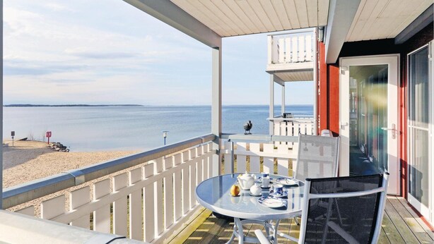 Un balcon avec une table dressée pour le thé, donnant sur une plage et la mer.