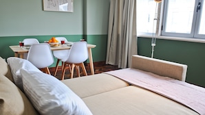A hotel room with a bed, a dining table with chairs, and a window with curtains. - Cosmopolitan Comfort in Lisbon (4A)- by Misha's Pl (Lisboa ciudad)