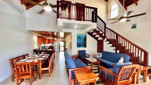 Un espacio habitable amplio con techo alto, muebles de madera, un comedor y una escalera que lleva a un nivel superior.