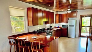 Una cocina moderna con armarios de madera, una isla central con taburetes de bar, un refrigerador y un ventanal con vistas al verdor.