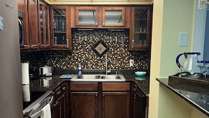 Una cocina con armarios de madera, salpicadero de azulejos, pileta de acero inoxidable y alfombra estampada.
