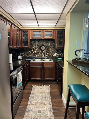 A kitchen with wooden cabinets, a tiled backsplash, a stainless steel sink, and a patterned rug.