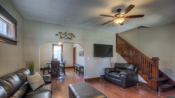 A spacious living room with a wooden staircase, leather sofas, and a ceiling fan.