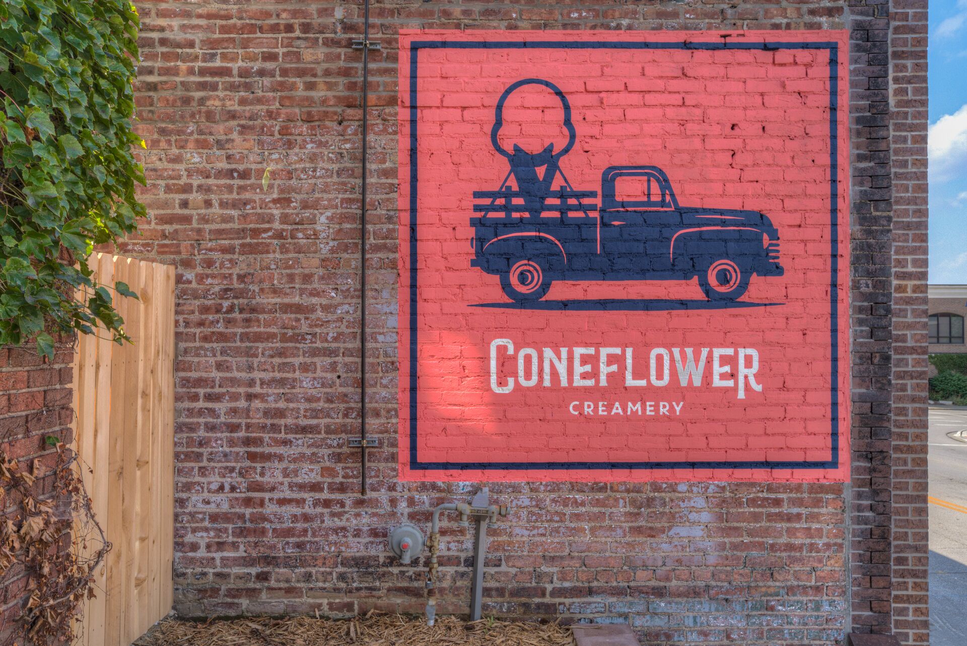 A brick wall with a painted mural of a vintage truck and the text "Coneflower Creamery".