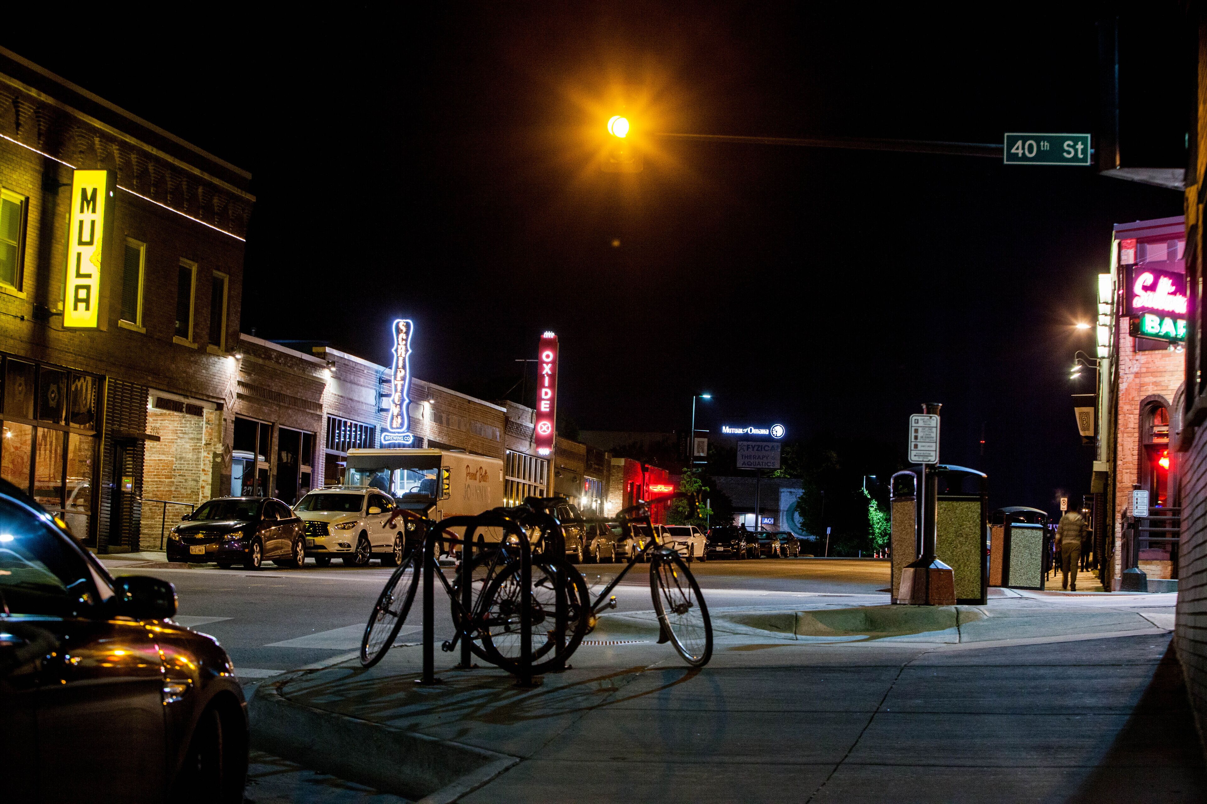 A street scene at night with buildings, a bicycle rack, and a street sign.