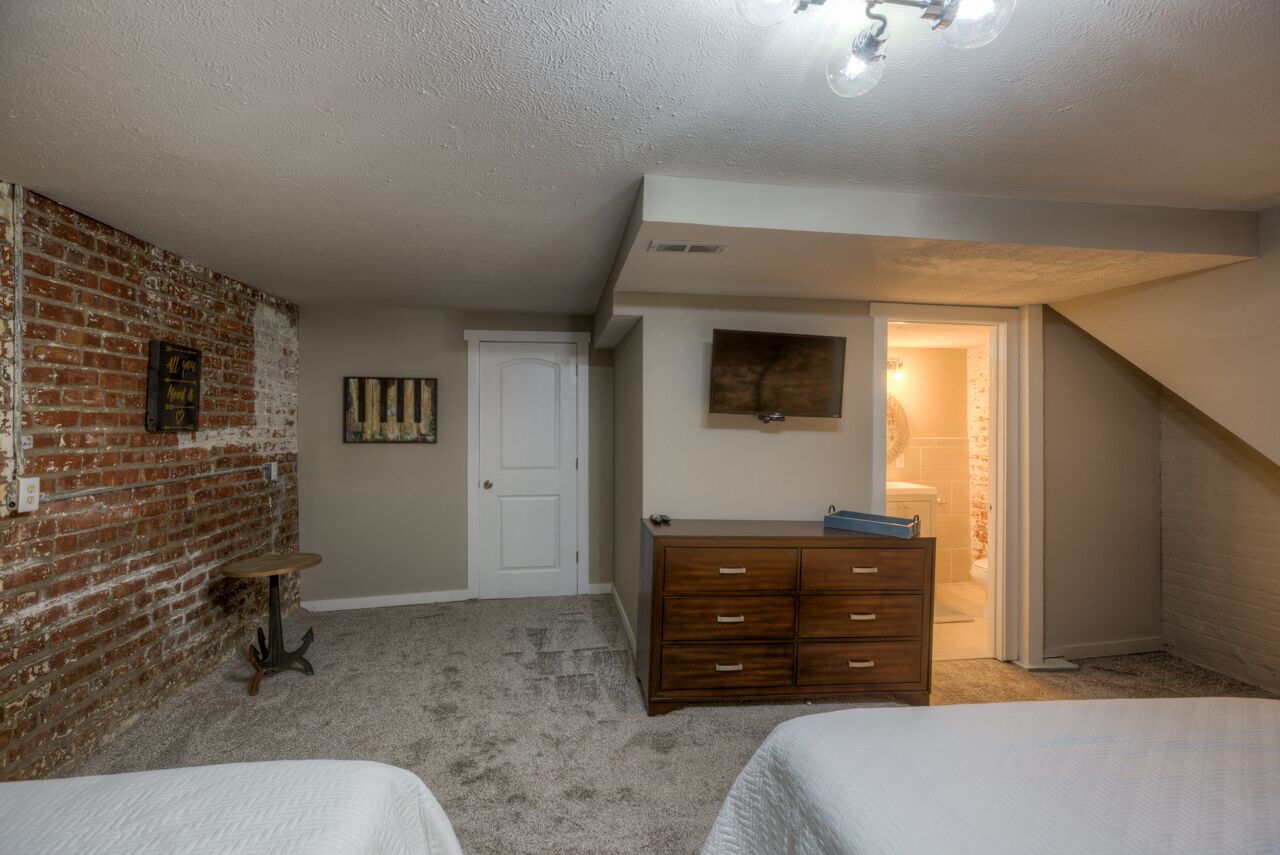 A bedroom with a brick wall, a white door, a dresser, and two beds.