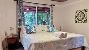 Una cama con una colcha estampada, una mesita de noche con una lámpara y una ventana con cortinas.