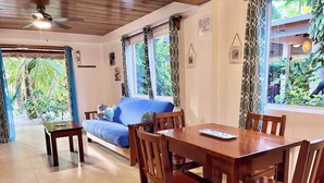 Una habitación con una mesa de comedor de madera, cuatro sillas, un sofá azul y un ventilador de techo.