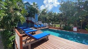 Un área de piscina con sillas reclinables azules y una terraza de madera.