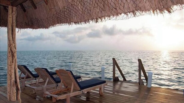 Una terraza de madera con sillones de descanso frente al mar, un techo de paja y una barandilla.