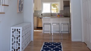 Un vaste espace de vie agrémenté d’un escalier en bois, une cuisine avec des meubles blancs et un tapis à motifs bleus.