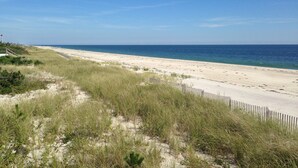 Une plage avec une clôture en bois, des dunes de sable et un ciel bleu dégagé.