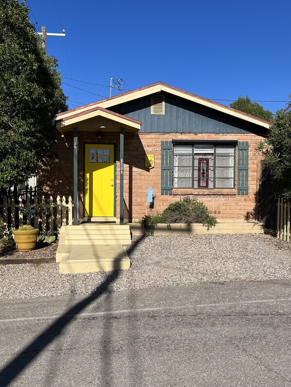 A two-story house with a yellow front door, a small porch, and a brick exterior. - LA CASITA: Charm/Privacy, Stunning Patio, pet friendly (Bisbee)