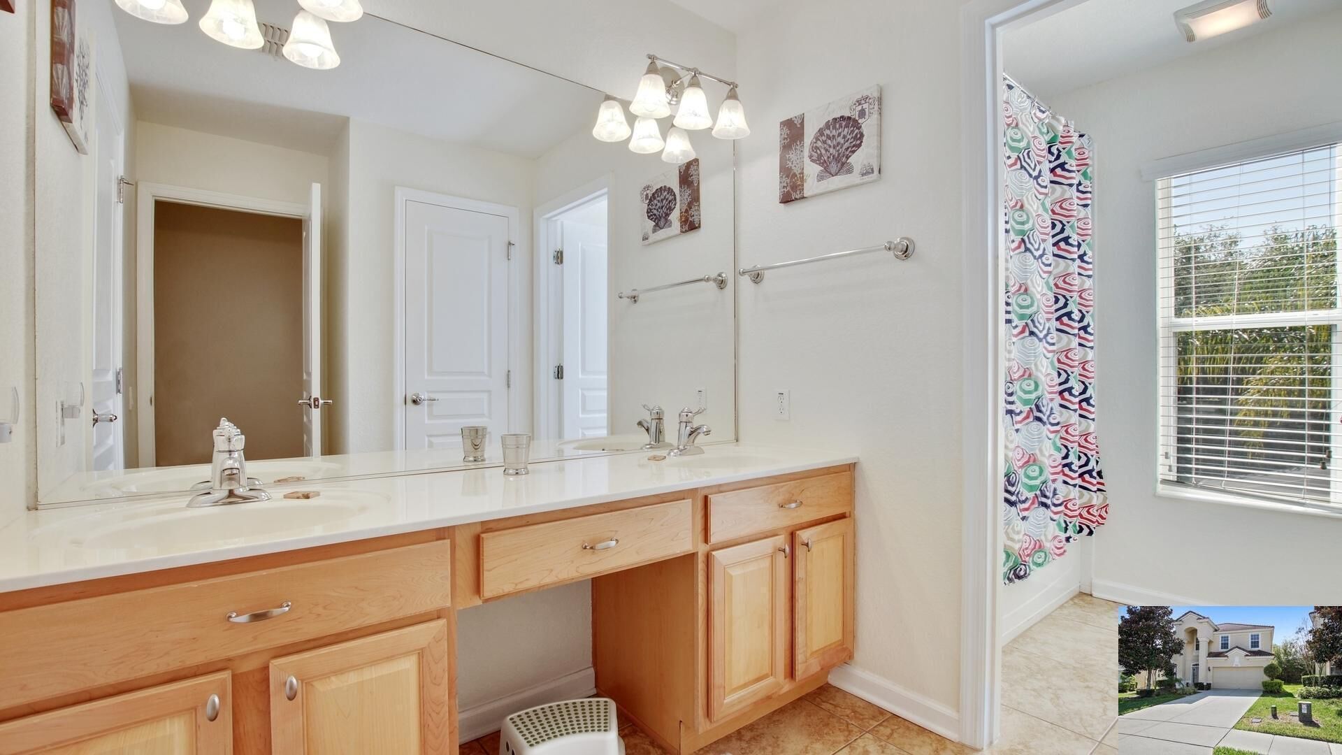 A bathroom with a large mirror, a sink, and wooden cabinets. There are decorative wall hangings and a window with blinds.