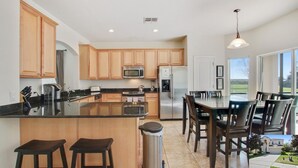 A modern kitchen with wooden cabinets, stainless steel appliances, and a central island with stools. - 6BR Family Retreat Near Disney | Pool + Arcade + Resort Access (Kissimmee)