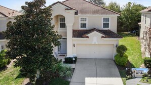 A two-story house with a tiled roof, a garage, and a well-maintained lawn. - 6BR Family Retreat Near Disney | Pool + Arcade + Resort Access (Kissimmee)