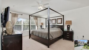 A four-poster bed with a dark finish, a ceiling fan, and a large window with blinds. - 6BR Family Retreat Near Disney | Pool + Arcade + Resort Access (Kissimmee)