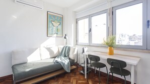 Una sala de estar moderna con un sofá, una mesita, dos sillones, una planta en maceta y un ventanal con vistas a la ciudad.