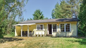 Et gult hus med tegltag, en veranda med stole og et lille bord.