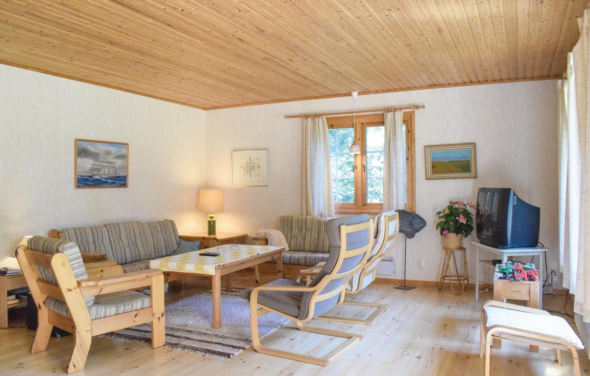 Un salon chaleureux avec un plafond en bois, un canapé, une table à manger avec des chaises, un téléviseur et des œuvres d’art accrochées aux murs.