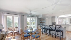 A spacious kitchen with a dining area, large windows, and a ceiling fan.
