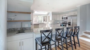 A modern kitchen with white cabinets, a large island with bar stools, and a skylight.