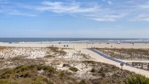 A beach with a paved path, dunes, and the ocean in the background.