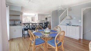 A modern kitchen with white cabinets, a dining table with blue cushioned chairs, and a ceiling fan.
